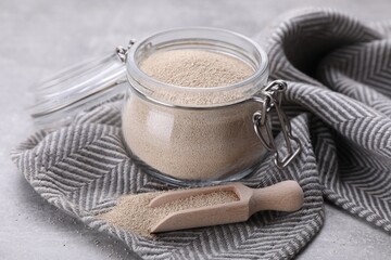 Glass jar and scoop with active dry yeast on light grey table, closeup