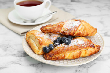 Fresh tasty puff pastry with sugar powder and blueberries served on white marble table, closeup