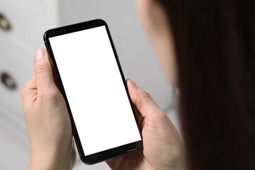 Woman holding smartphone with blank screen indoors, closeup. Mockup for design