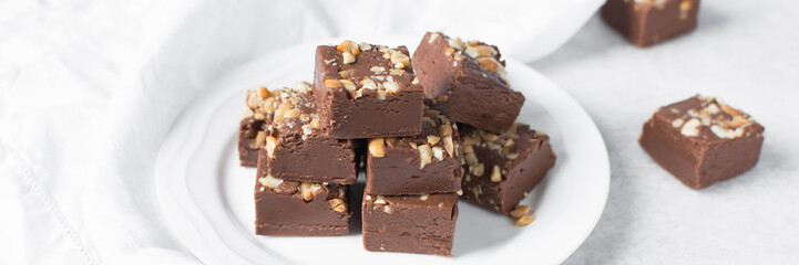chocolate fudge with nuts on a white ceramic plate, chocolate fudge cut into pieces, fudge candy on a plate