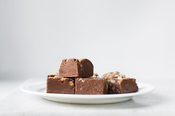 chocolate fudge with nuts on a white ceramic plate, chocolate fudge cut into pieces, fudge candy on a plate