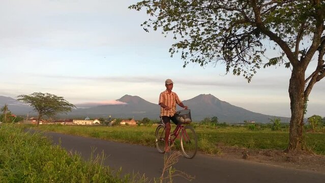 Man riding a bike at the village with beautiful mountains and rice field as background.
