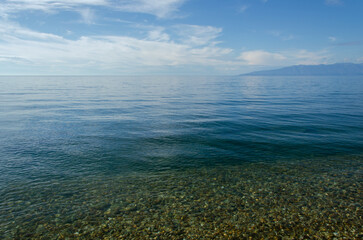 Fototapeta na wymiar Lake Baikal on a sunny summer day. The smooth surface of the lake merges with the horizon.