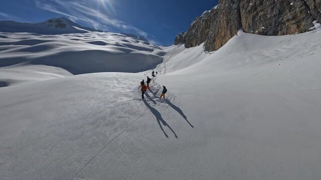 Ski tour heliski group standing ob big rock wall. Extreme sport tourist skiing snowboarding break riding snow mountain aerial view FPV drone shot travel expedition freeride winter cliff valley scenery