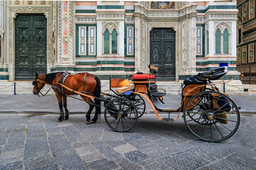 Fototapeta na wymiar Horse drawn carriage by the colored marble facade of Duomo Cathedral or Cattedrale di Santa Maria del Fiore in Florence, Italy waiting for tourists