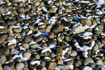 Textures in nature, snow covered river rocks on a sunny winter day, as a nature background
