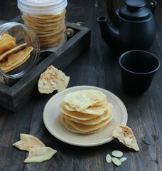Crispy almond biscuits on a white plate on a black teapot background
