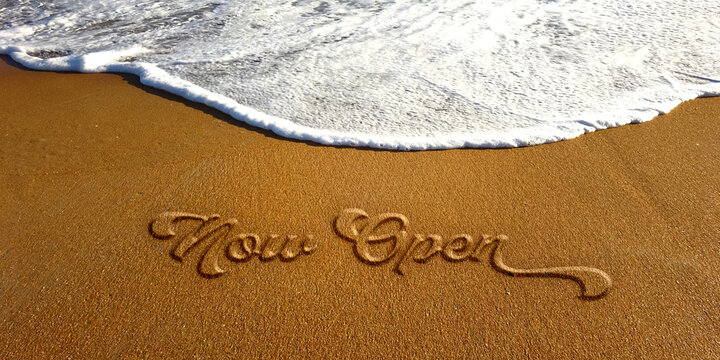 Now Open text sign embossed lettering on the sand beach with white ocean wave. photo image