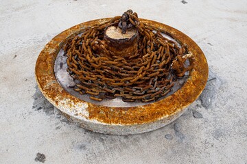 Rusted metal chain coiled around base on a light gray stone dock at a marina.