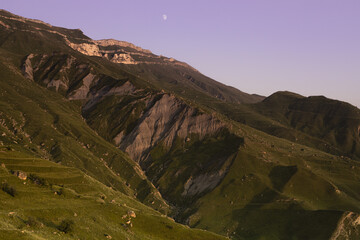 Amazing summer mountain landscape with green folded mountain ridge with rocky cliffs and moon in...