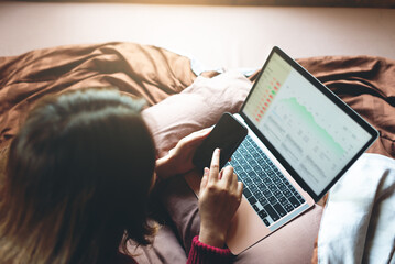 Young businesswoman checking stock chart on bed in his house