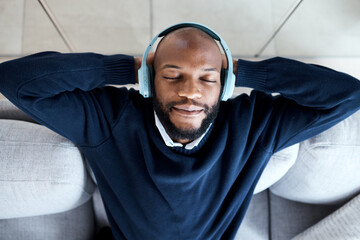 Top view, music headphones and black man on sofa in home living room streaming audio. Meditation,...