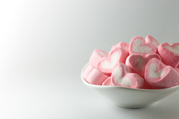 Pink and white heart shaped marshmallows in a white container with copy space on the left.