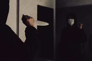 The back of a knife-wielding murderer in a dark bathroom looks grim as he is about to injure the...