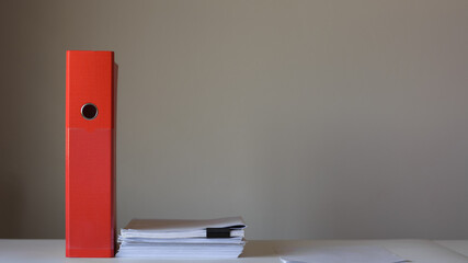 Red folder and stack of papers on empty wall background.