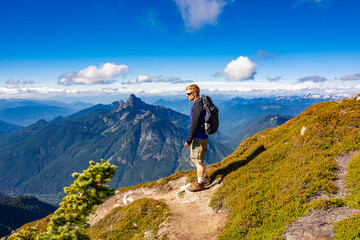 Adventurous athletic male hiker standing on a hiking trail on top of a rugged mountain in the...