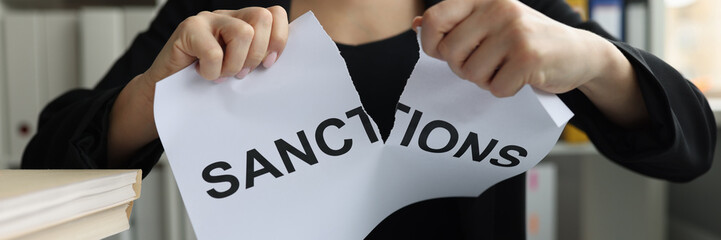 Businesswoman tears up sheet of paper with sanctions inscription