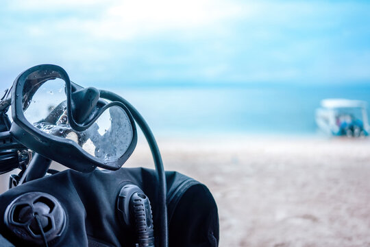Background for a diving school. Black diving goggles are hanging from diving equipment in the foreground. In the blurred background is sea, blue sky, beach and a boat as copy space