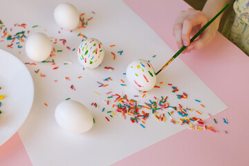 A ten-year-old girl decorates an egg for Easter. Acrylic paints and brush. Close-up.
