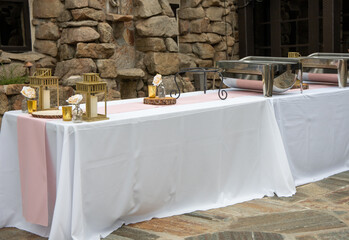 Long table setup for buffet with white table covers, pink runner, chafers and candles. Rental party...