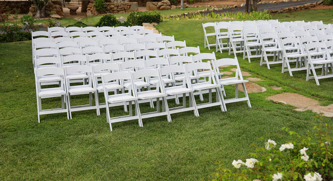 Rows of white resin folding chairs with padding aligned for wedding ceremony.