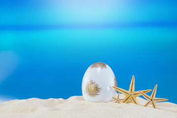 White gold egg with starfish on sandy beach of sea or ocean. Holiday postcard in sunny country....