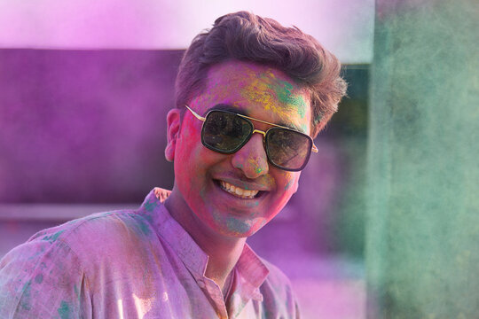 close-up portrait of smiling young man with colourful face and sunglass on holi