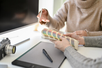 Fototapeta premium Two creative female graphic designers working together in the office, choosing colors on color chart.