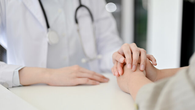 Close-up image of a caring female doctor holding a patient's hands to comfort her during the meeting