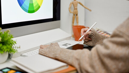 Side view of a female graphic designer working at her desk, using computer and graphic tablet