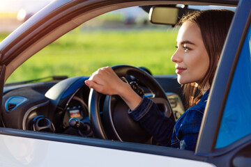 Close-up portrait young woman with joyful positive expression, satisfied with an unforgettable trip by car, sits on the driver's seat, hands on the steering wheel. People driving, transport concept