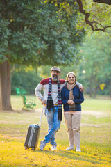 Indian Senior couple with travel bag at park.