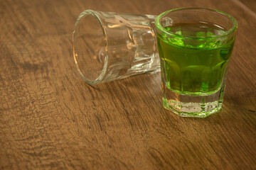 shot glasses lined up on wooden bar background filled with green spirit cocktail and shamrock,...