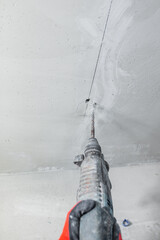 Builder electrician makes a hole puncher in a concrete wall for installation of electrical cables -...