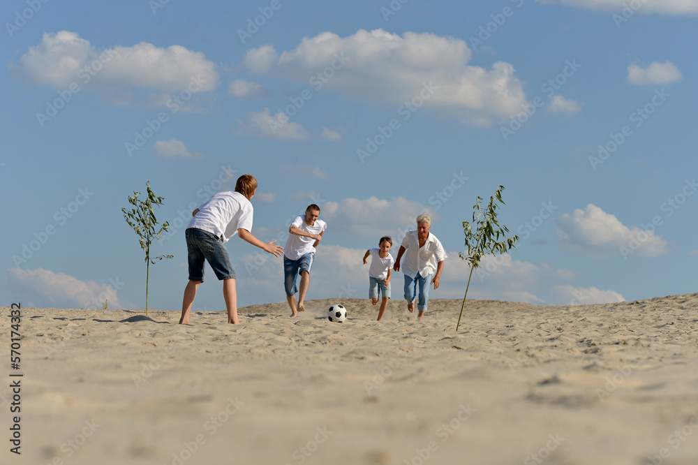 Poster family playing football on a beach in summer day