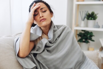 Woman cold headache with a cup of tea sits on a sofa in a plaid, treatment for flu, allergies and covid-19