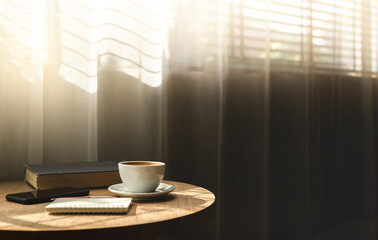 Close up view, white coffee cup with old book and smart phone on wooden table near bright window and the sun is shining through, vintage color tone
