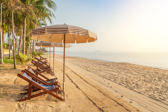 Row of empty wooden beach deck chairs with parasols on tropical sandy beach in the morning , leisure summer holidays concept 