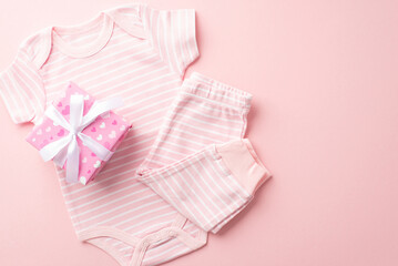 Gender reveal party concept. Top view photo of pink giftbox with ribbon bow infant clothes bodysuit and pants on isolated pastel pink background