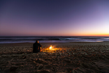 Rear view of a lonely guy and bonfire on the beach at sunset
