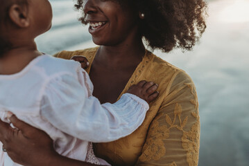 Close up detail of daughters hands embracing mother at beach