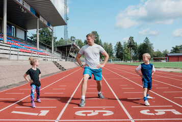 father doing stretches with his kids on a race track