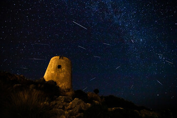 Perseid meteors shower and Milky Way and medieval tower in foreground
