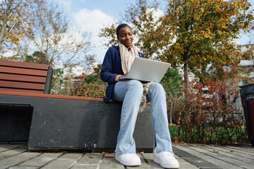 Young african businesswoman using laptop while sitting on the bench in the city