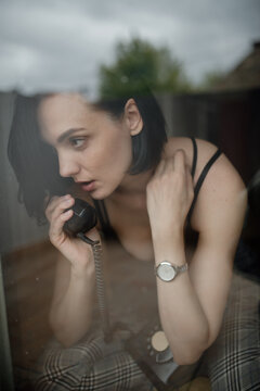 Woman behind the window talking on a rotary telephone.