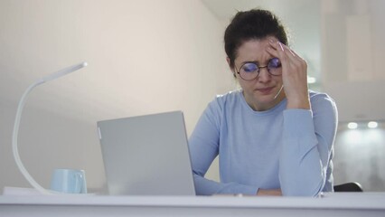 Young woman office worker typing on laptop and feeling headache, migraine