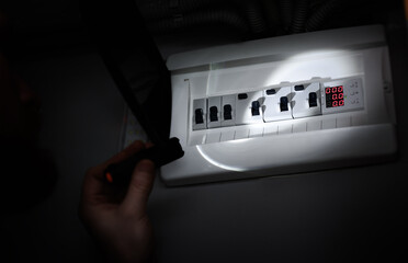 a hand shines a flashlight into an electrical panel with a circuit breaker. power outage. blackout