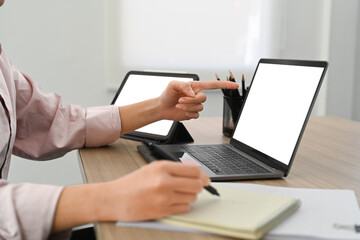 Fototapeta premium Cropped image of businesswoman pointing on laptop screen and writing on notepad