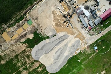 A top-down view of a stationary concrete batching plant. The image shows various building structures, equipment, and materials used in the production of concrete aggregate