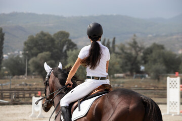 A young slender girl rider is engaged in horseback riding.